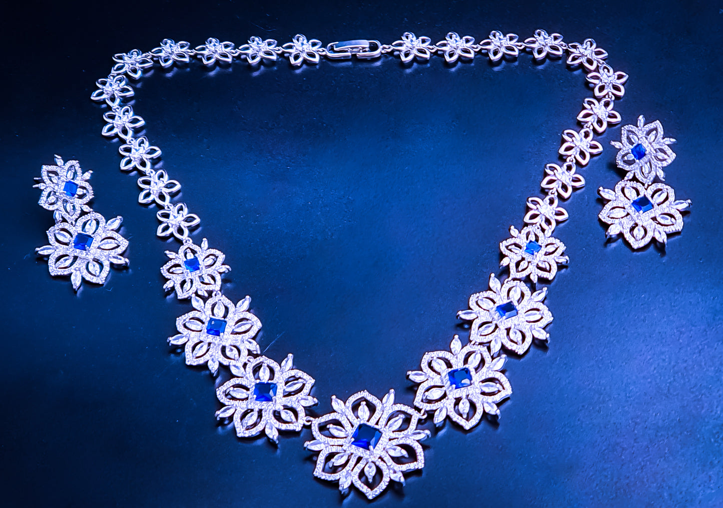 Titanium Steel Cubic Zirconia Necklace Set - Introducing Raani's Regal Blue Necklace Set, crafted with rhodium-finish Titanium Steel and Cubic Zirconia. This enchanting ensemble features a delicate floral design adorned with blue and white cubic zirconia that sparkle like stars in the night sky.